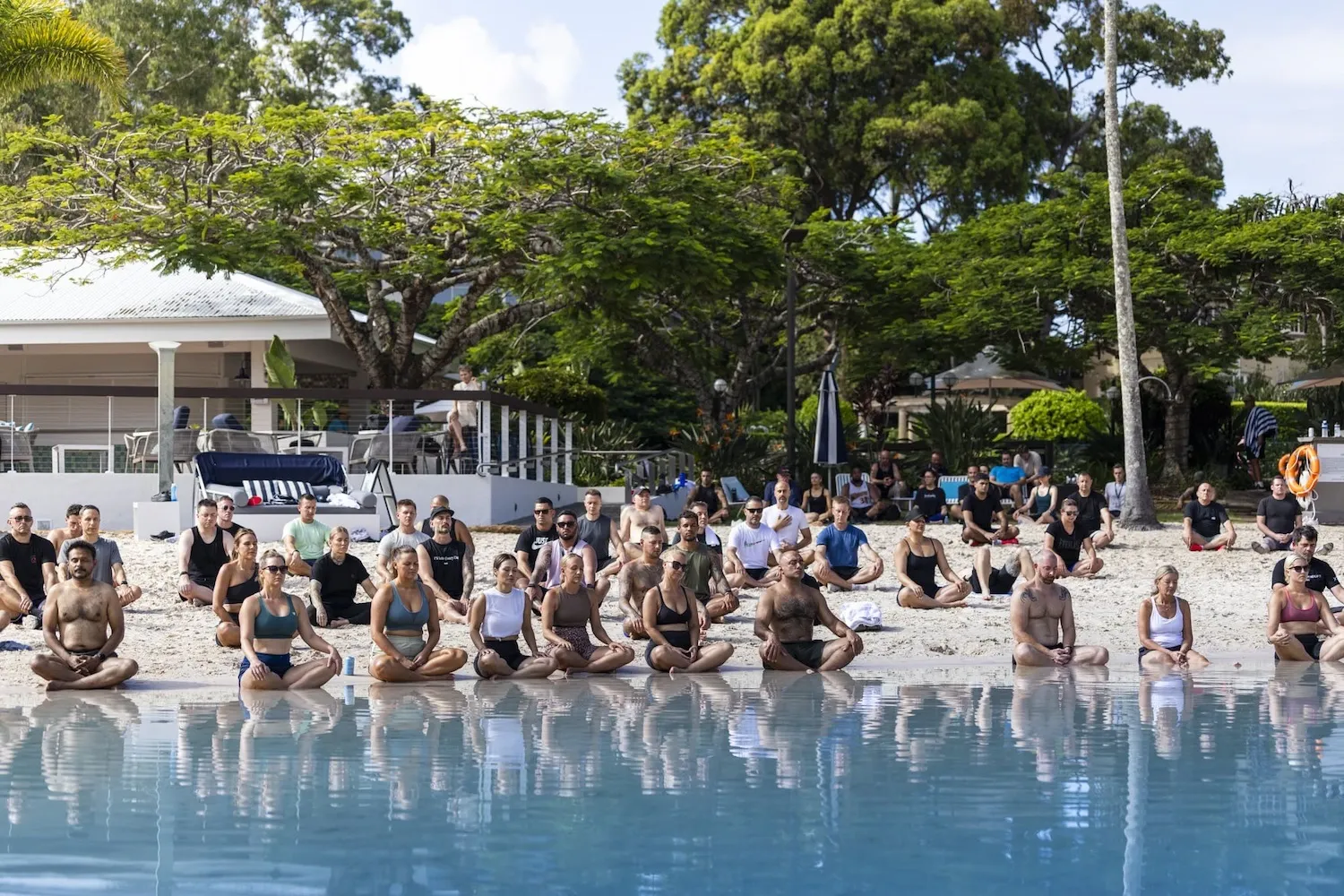 Members in a poolside group meditation at a One Life Club health and wellness day